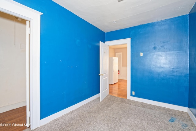 unfurnished bedroom featuring baseboards, freestanding refrigerator, and carpet