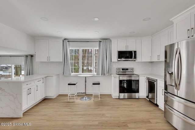 kitchen with stainless steel appliances, a peninsula, white cabinetry, decorative backsplash, and light wood finished floors