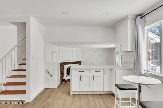 kitchen featuring light wood finished floors, a peninsula, light stone countertops, white cabinetry, and backsplash