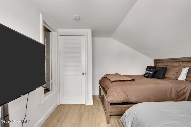 bedroom with light wood-style floors, lofted ceiling, and baseboards