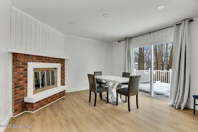 dining area with a brick fireplace, light wood-style flooring, and baseboards