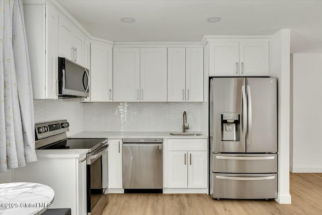 kitchen with stainless steel appliances, a sink, light countertops, and white cabinetry