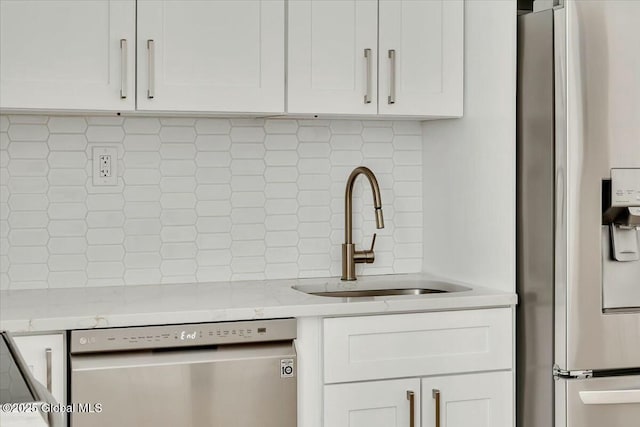 kitchen featuring stainless steel appliances, backsplash, a sink, and white cabinetry