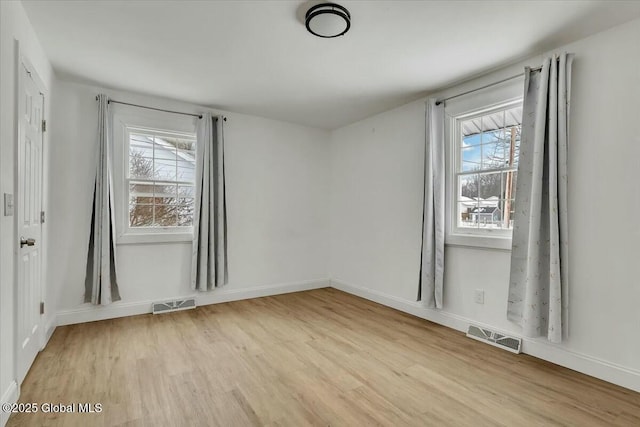 empty room featuring light wood-style floors, baseboards, and visible vents