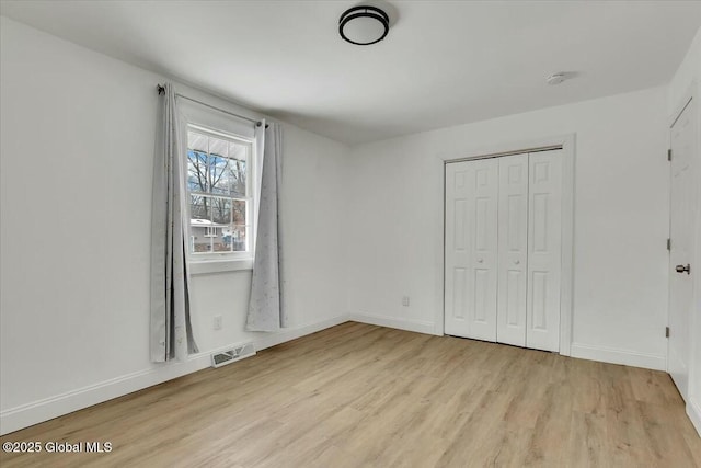 unfurnished bedroom with baseboards, a closet, visible vents, and wood finished floors