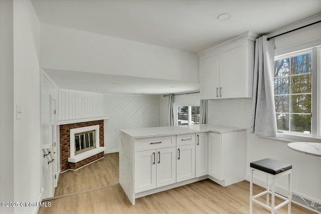 kitchen with a peninsula, light wood finished floors, plenty of natural light, and white cabinets