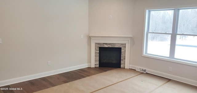 unfurnished living room with visible vents, a stone fireplace, baseboards, and wood finished floors