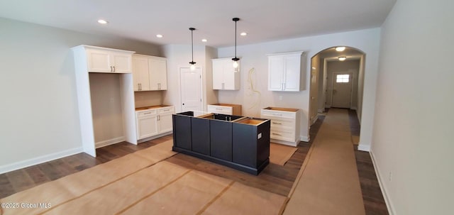 kitchen with arched walkways, hanging light fixtures, a kitchen island, and white cabinetry