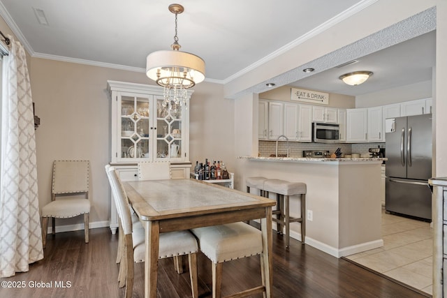 dining room featuring baseboards, ornamental molding, wood finished floors, and a notable chandelier