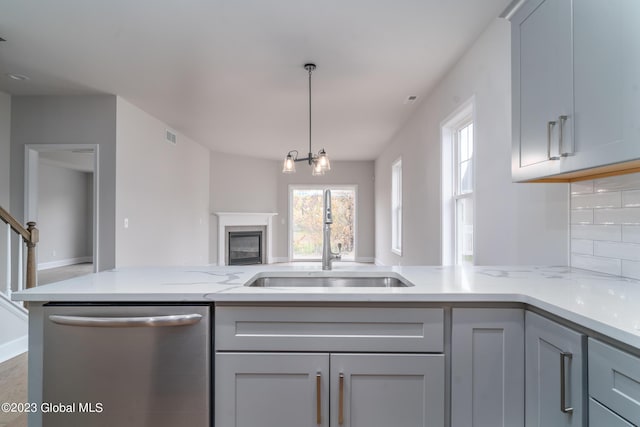 kitchen with gray cabinetry, a sink, open floor plan, stainless steel dishwasher, and light stone countertops