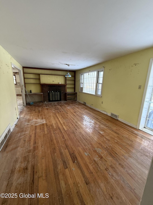 unfurnished living room featuring a brick fireplace, visible vents, baseboards, and wood finished floors