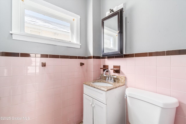 half bath featuring toilet, wainscoting, vanity, and tile walls