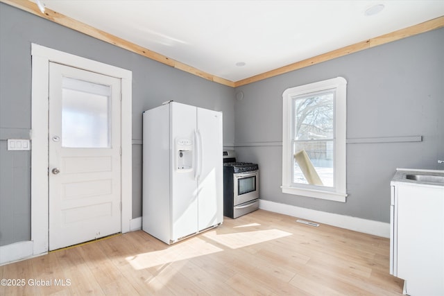 kitchen with white refrigerator with ice dispenser, visible vents, stainless steel gas stove, light wood-type flooring, and baseboards