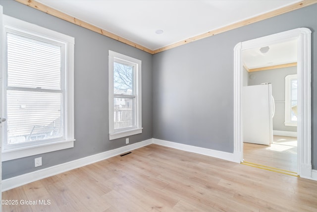 unfurnished room with light wood-style flooring, visible vents, baseboards, and crown molding