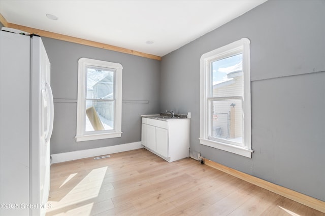 spare room with plenty of natural light, baseboards, light wood-style flooring, and a sink