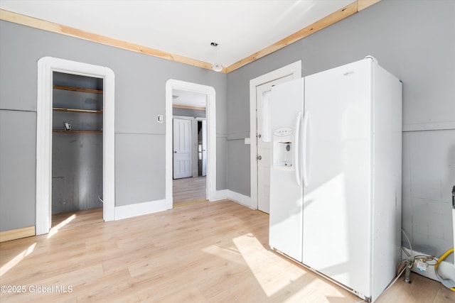 unfurnished bedroom featuring light wood finished floors, white refrigerator with ice dispenser, and baseboards