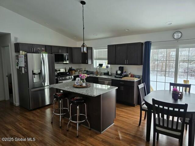 kitchen featuring a kitchen island, stainless steel appliances, dark cabinetry, and decorative light fixtures