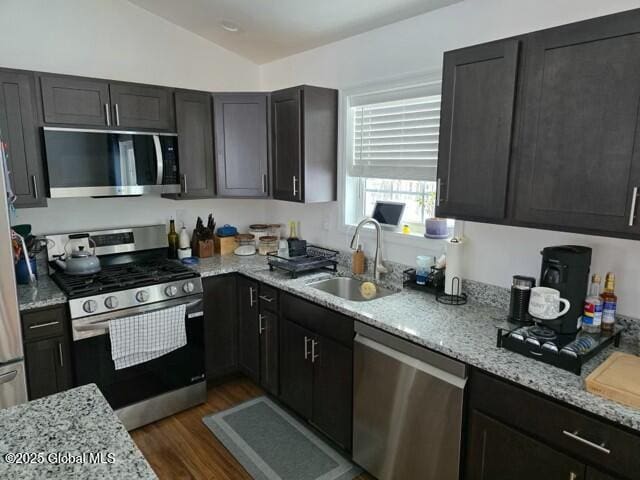 kitchen featuring dark wood-style floors, stainless steel appliances, vaulted ceiling, a sink, and light stone countertops