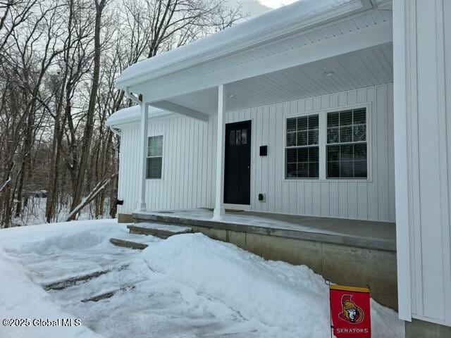 snow covered property entrance with a porch and board and batten siding