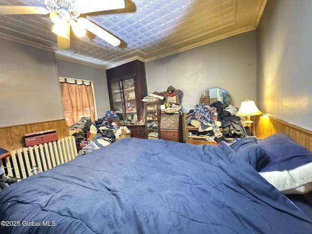 bedroom with a wainscoted wall, wood walls, a ceiling fan, an ornate ceiling, and crown molding