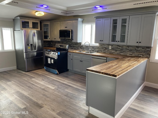 kitchen featuring glass insert cabinets, appliances with stainless steel finishes, a peninsula, wooden counters, and a sink