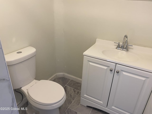 half bathroom featuring toilet, vanity, and baseboards