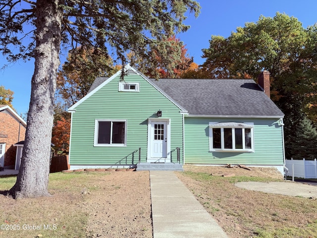 bungalow-style home featuring a shingled roof, a chimney, fence, and a front yard