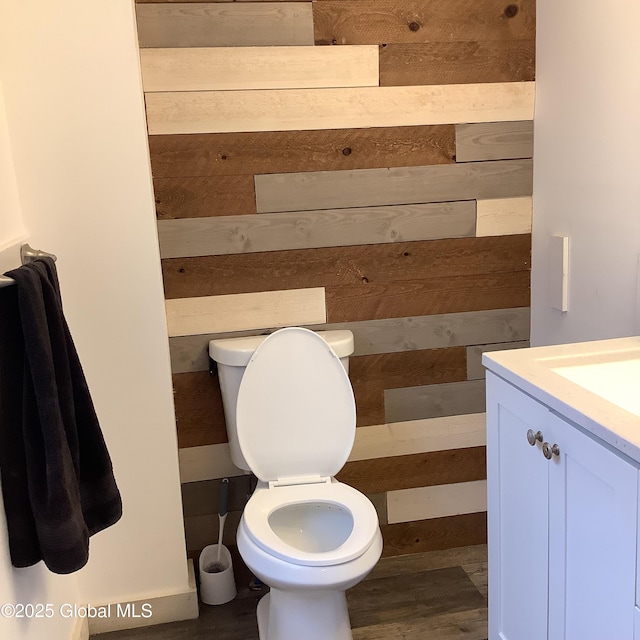 bathroom featuring wooden walls, toilet, and vanity