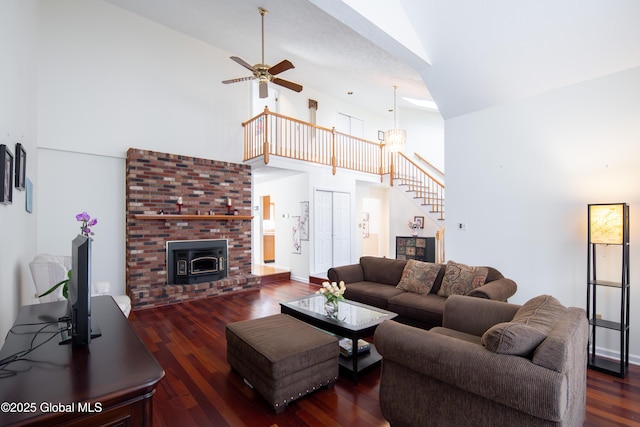 living area with dark wood finished floors, a ceiling fan, stairs, a brick fireplace, and high vaulted ceiling