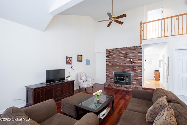 living area with a wood stove, ceiling fan, wood finished floors, high vaulted ceiling, and baseboards