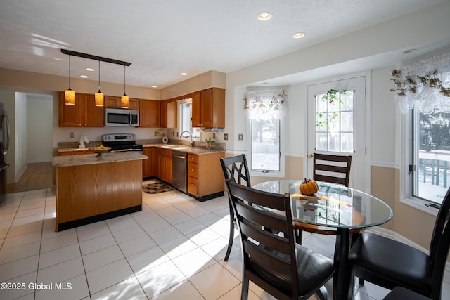 kitchen featuring appliances with stainless steel finishes, brown cabinetry, a sink, and decorative light fixtures