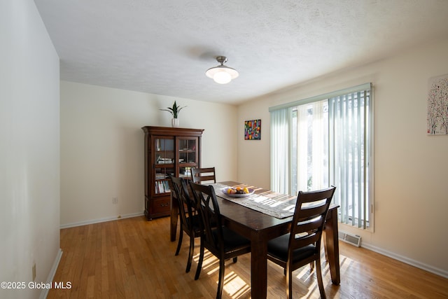 dining room featuring a textured ceiling, light wood finished floors, visible vents, and baseboards