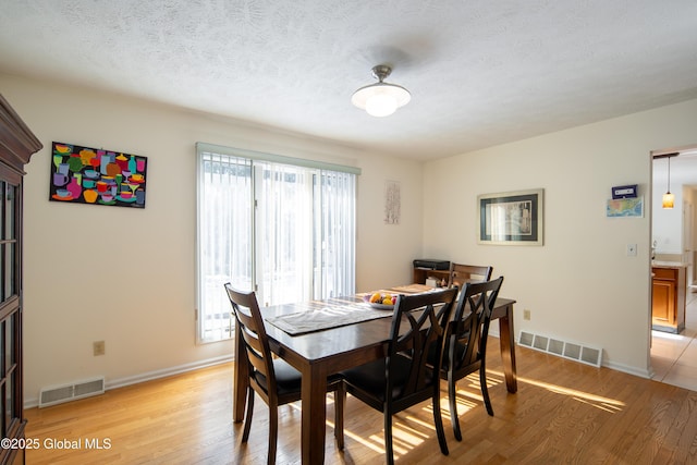 dining space with a textured ceiling, light wood finished floors, visible vents, and baseboards