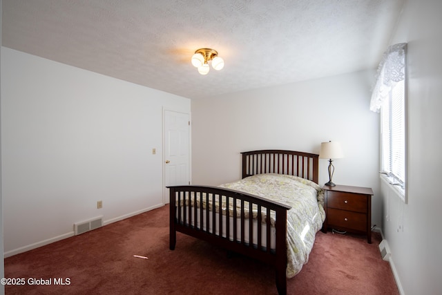 bedroom with a textured ceiling, dark colored carpet, visible vents, and baseboards