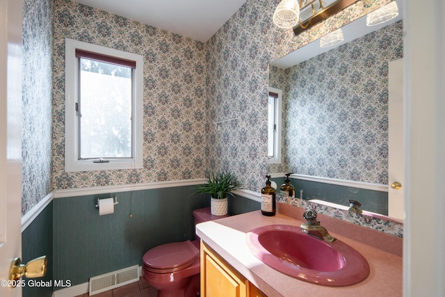 bathroom with visible vents, toilet, wainscoting, vanity, and wallpapered walls