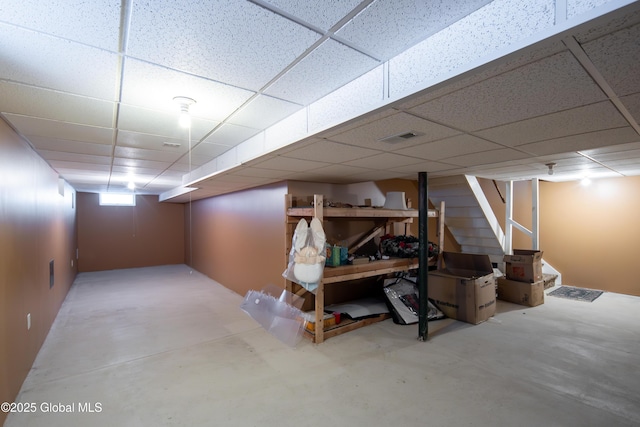 basement featuring stairs, a drop ceiling, and visible vents