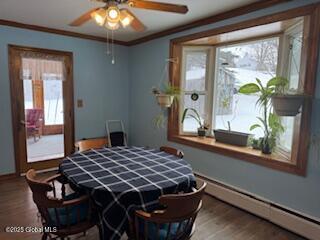 dining room with a ceiling fan, a baseboard heating unit, crown molding, and wood finished floors