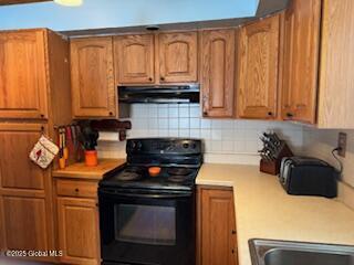 kitchen featuring tasteful backsplash, brown cabinets, black electric range oven, range hood, and light countertops