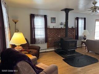 living room featuring a wood stove, ceiling fan, a baseboard heating unit, and wood finished floors