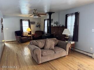 living area featuring a wood stove, light wood finished floors, ceiling fan, and baseboard heating