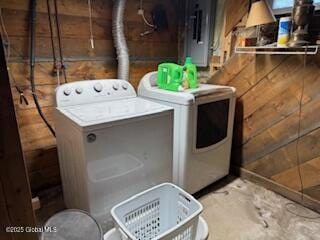 clothes washing area with laundry area, wooden walls, and washer and dryer