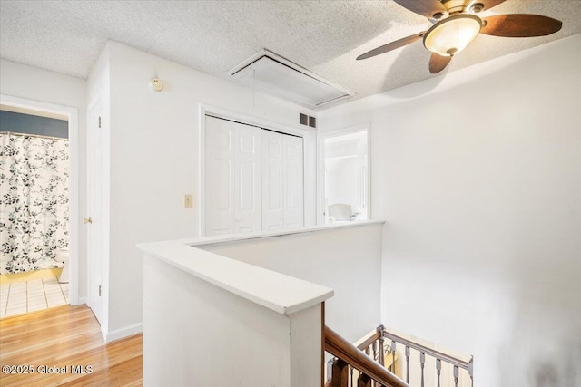 hallway with a textured ceiling, visible vents, an upstairs landing, light wood-style floors, and attic access