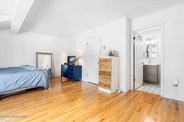 bedroom with beam ceiling, ensuite bath, and light wood finished floors