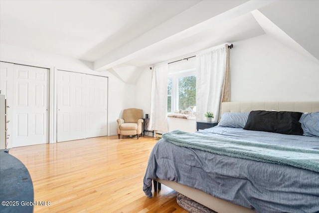 bedroom with a baseboard heating unit, vaulted ceiling with beams, two closets, and wood finished floors