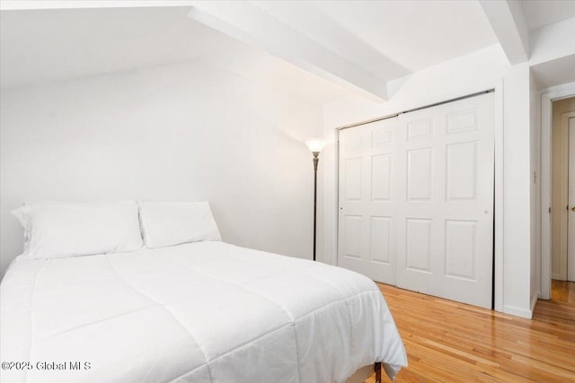 bedroom with a closet, wood finished floors, and beam ceiling