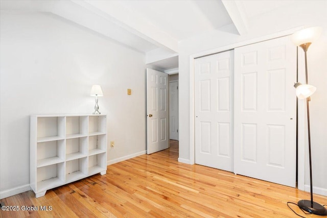 unfurnished bedroom featuring a closet, beam ceiling, baseboards, and wood finished floors