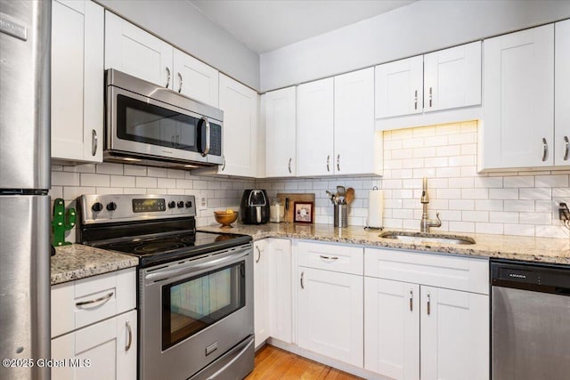 kitchen with tasteful backsplash, light stone counters, stainless steel appliances, white cabinetry, and a sink