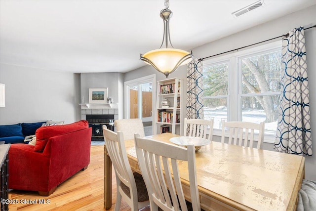 dining room with light wood finished floors, a fireplace, and visible vents