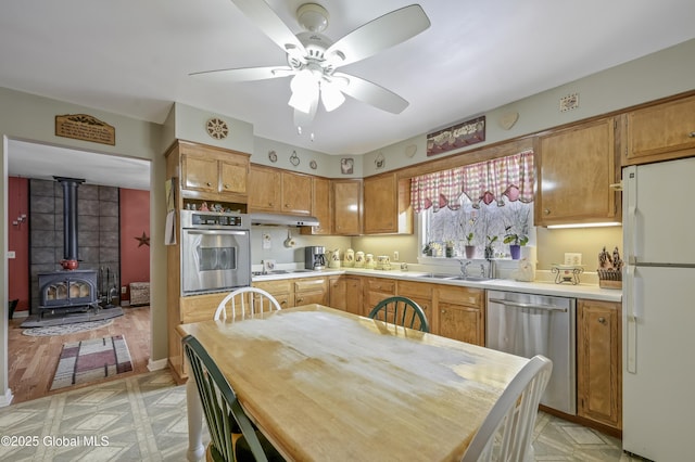 kitchen with appliances with stainless steel finishes, a wood stove, light countertops, light floors, and a sink