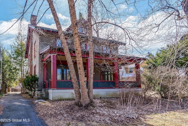 view of front facade featuring stucco siding, covered porch, and a chimney